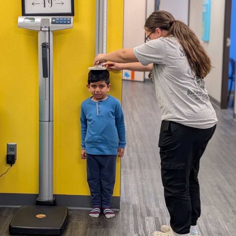 A medical assistant measures the height of a young patient
