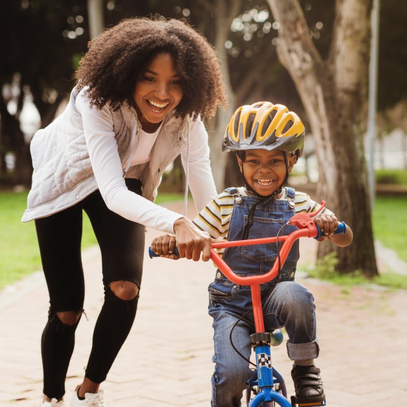 A Black mother teaches her son how to ride a bike