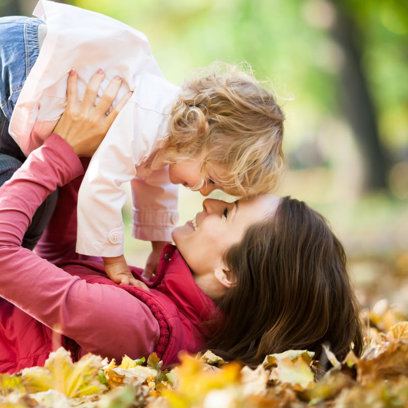 A mother play in the leaves with her young daughter